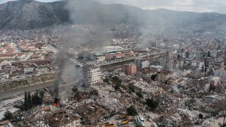 Smoke billows from the Iskenderun Port as rescue workers work at the scene of a collapsed building, Feb. 7, 2023, in Iskenderun, Turkey. A 7.8-magnitude earthquake hit near Gaziantep, Turkey, causing widespread destruction in southeastern Turkey and northern Syria.