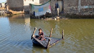 A girl sits on a cot as she crosses a flooded street at Sohbatpur in Jaffarabad district of Balochistan province in Pakistan on October 4, 2022.