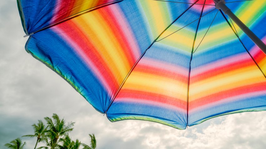 A colorful beach umbrella on a hot sunny day in the tropics. The warm sun penetrates through the awning of the umbrella. Coconut palms in the distance. This is paradise.