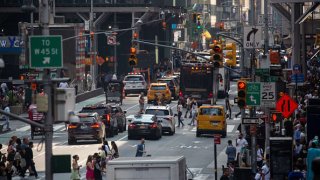 Pedestrians cross a street past traffic in the Midtown neighborhood of New York, June 17, 2023.