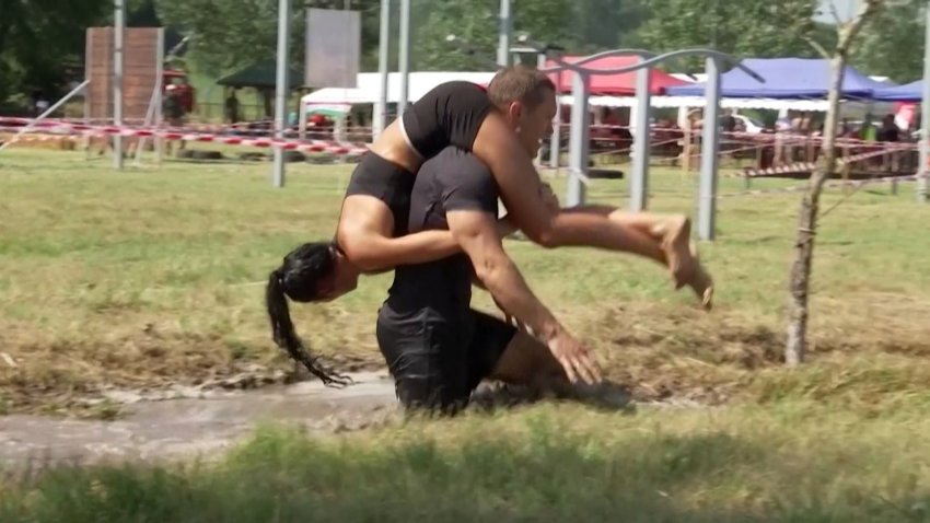 A man carrying his wife through an obstacle course.