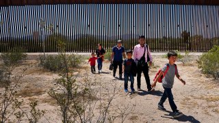 A family of five claiming to be from Guatemala and a man stating he was from Peru, in pink shirt, walk through the desert after crossing the border wall in the Tucson Sector of the U.S.-Mexico border, Tuesday, Aug. 29, 2023, in Organ Pipe Cactus National Monument near Lukeville, Ariz.