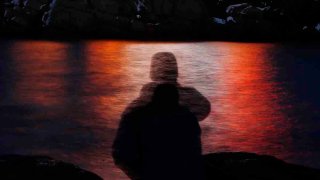 FILE - In this photo made with a long exposure, a man is silhouetted against lights reflected in the waters off Cape Neddick in Maine on Dec. 11, 2017.