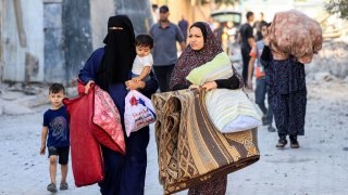 Palestinian women walk with children and belongings as they flee an area in the aftermath of an Israeli air strike in Rafah in the southern Gaza Strip on October 13, 2023. 