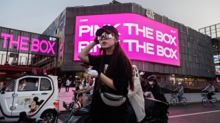 A woman waits on her bicycle to cross an intersection outside a new shopping mall in Beijing, China, on Sept. 13, 2023.