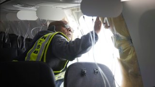 In this photo released by the National Transportation Safety Board, investigator-in-charge John Lovell examines the fuselage plug area of Alaska Airlines Flight 1282 in Portland, Oregon, on Jan. 7, 2024.