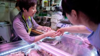 A butcher (L) shows a piece of pork to a customer at a market in Beijing on July 10, 2019.