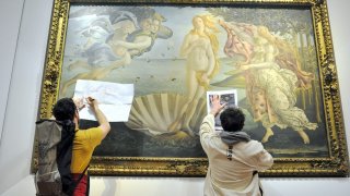 Protesters from the action group Ultima Generazione stick a sign and photographs of floods on the glass covering Sandro Botticelli's La nascita di Venere (Birth of Venus)