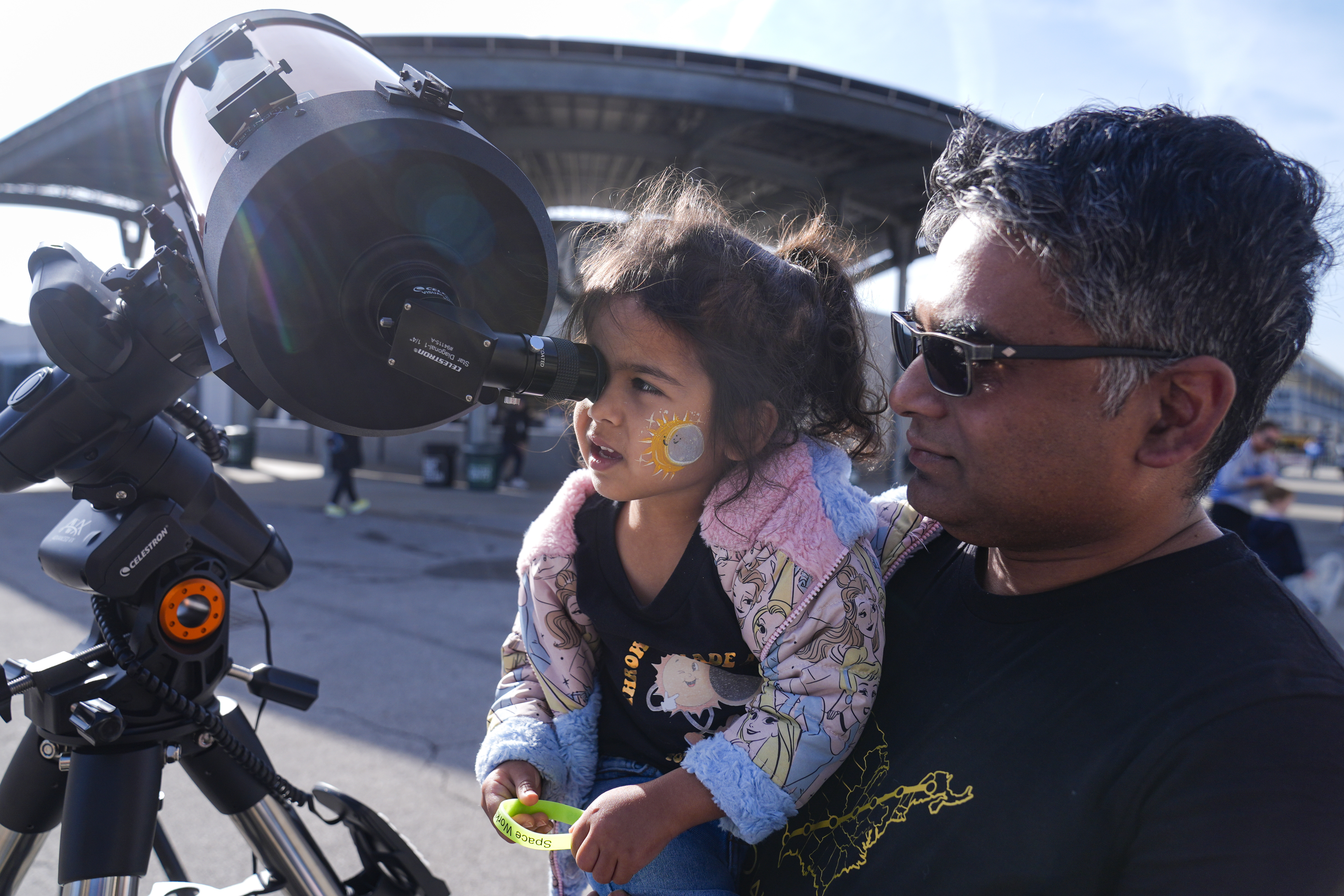 Tawhid Rana, of Midland, Mich., hold his daughter Thia, as she views the sun through a telescope at the Indianapolis Motor Speedway in Indianapolis, Monday, April 8, 2024.