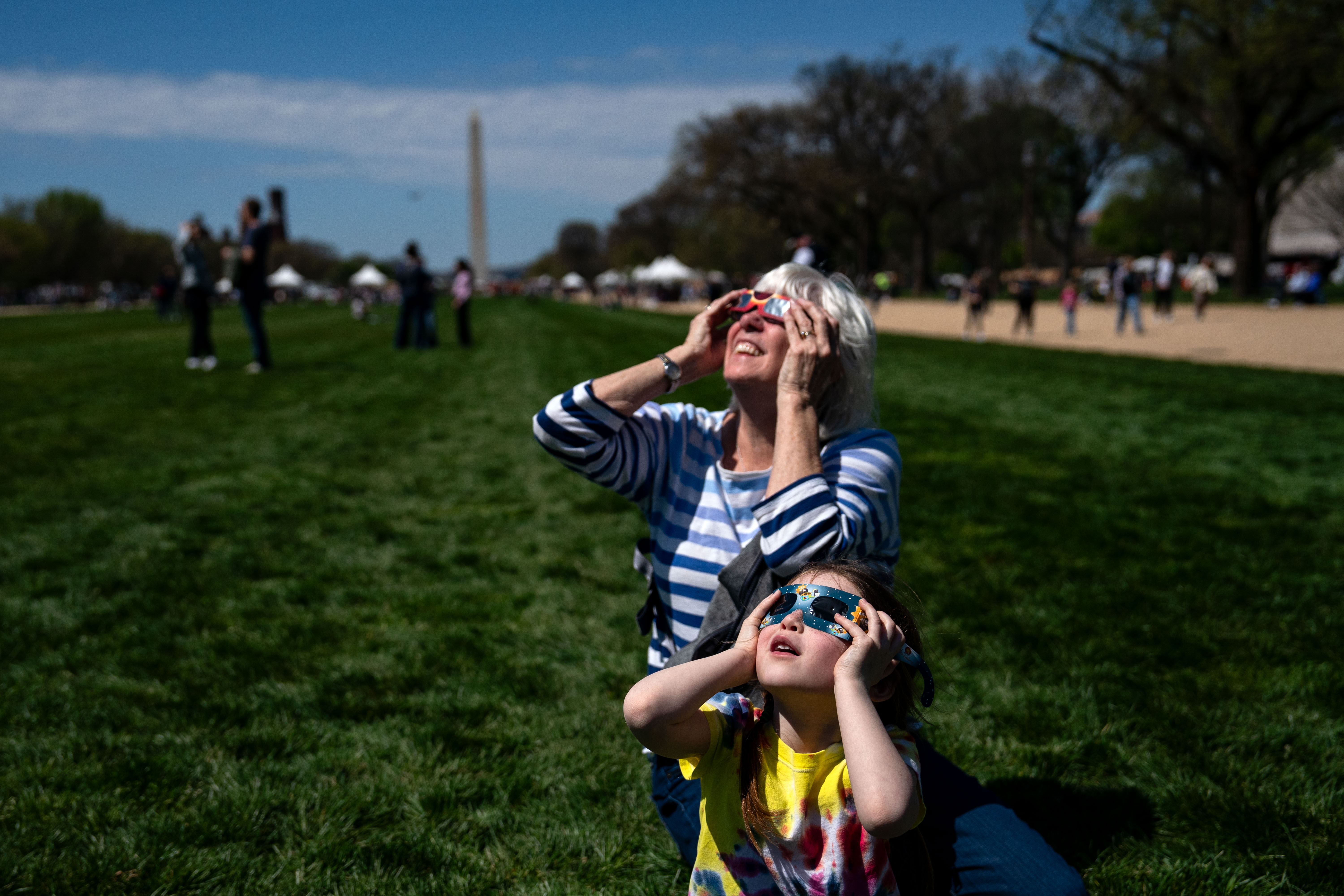 Barbara McLaughlin from Washington, DC, and her granddaughter test out their eclipse viewing glasses by looking towards the sun as they and people gather on the National Mall to view the partial solar eclipse on April 8, 2024 in Washington, DC.