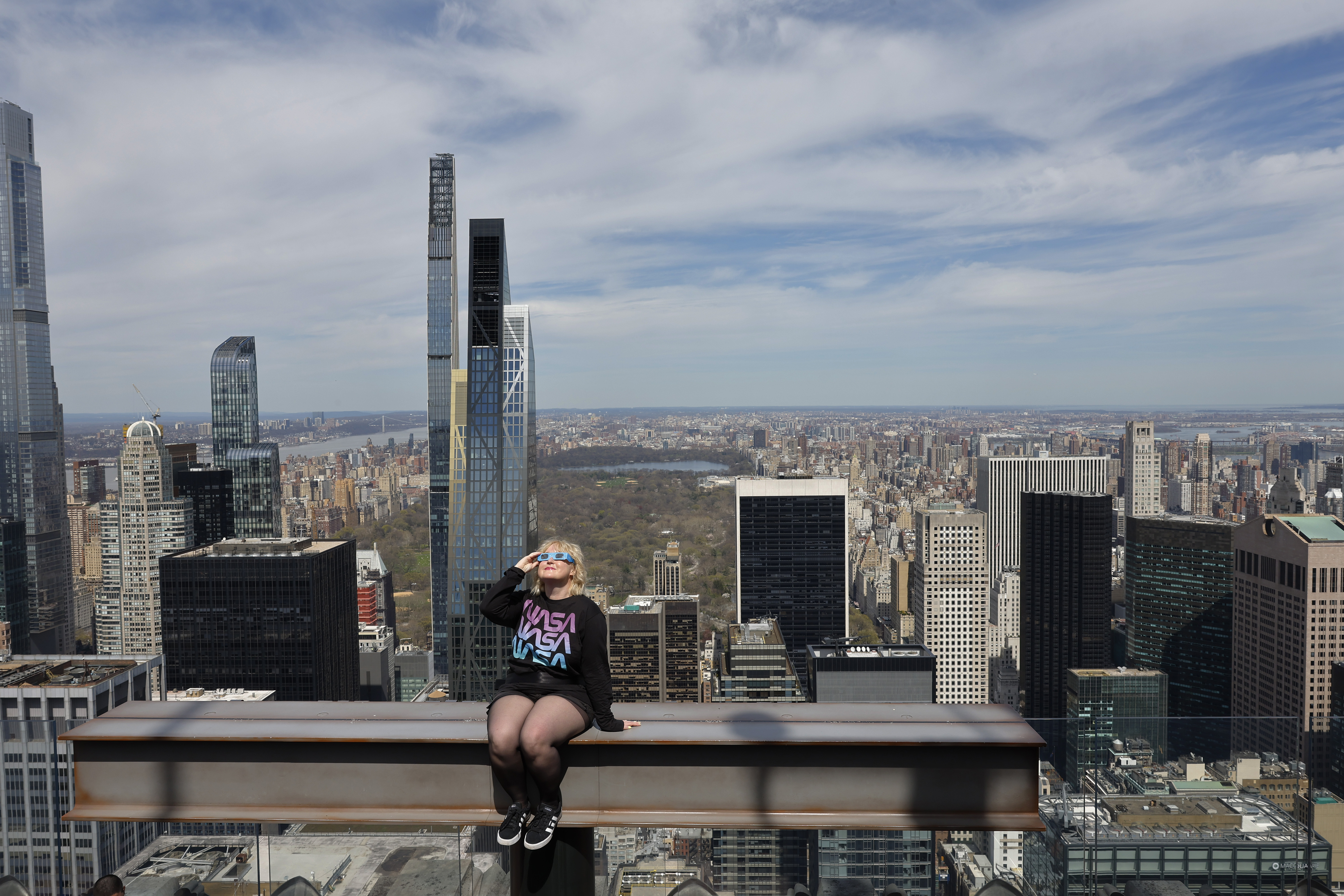 Laura Holden poses for a photo wearing eclipse glasses at the Beam as she prepares to watch a partial solar eclipse from the Top of the Rock at Rockefeller Center on April 08, 2024 in New York City.