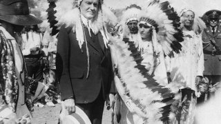 FILE – U.S. President Calvin Coolidge wears a Native American headdress of the Sioux tribe as he is adopted as Chief Leading Eagle and first white chief of the tribe at the celebration of the 51st anniversary of the settlement of Deadwood, South Dakota, in 1927. Coolidge signed the Indian Citizenship Act of 1924.