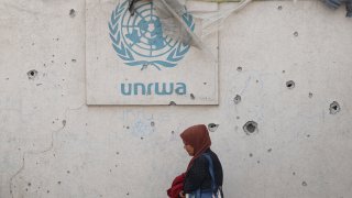 A Palestinian woman walks past a damaged wall bearing the UNRWA logo