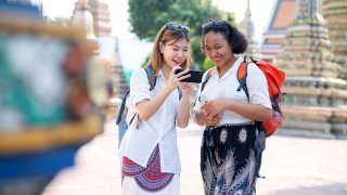 Female travelers viewing travel information via mobile apps during their visit to Wat Pho, Bangkok, Thailand.