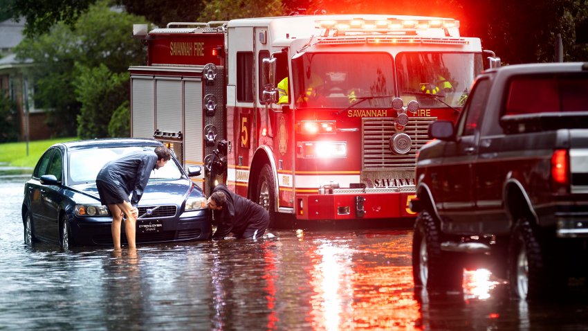 People attach a towline to a stranded vehicle on a flooded street after heavy rain from Tropical Storm Debby, Monday, Aug. 5, 2024, in Savannah, Ga.