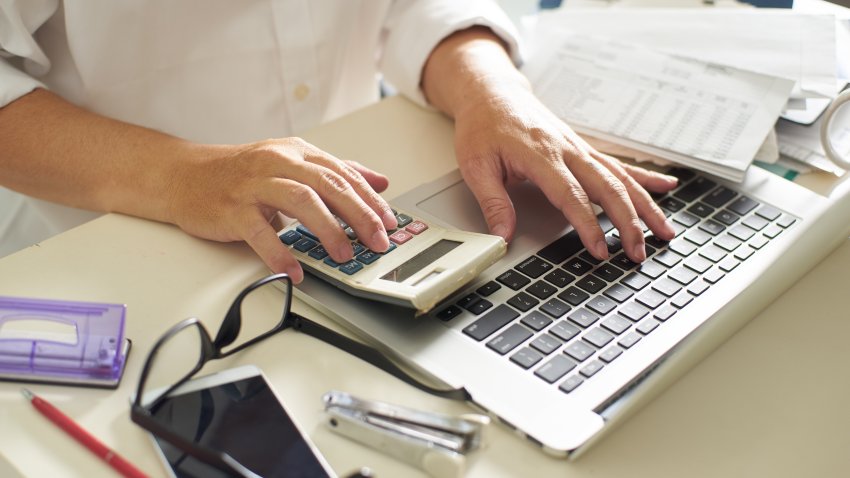 Person working with calculator and laptop on the white table at office