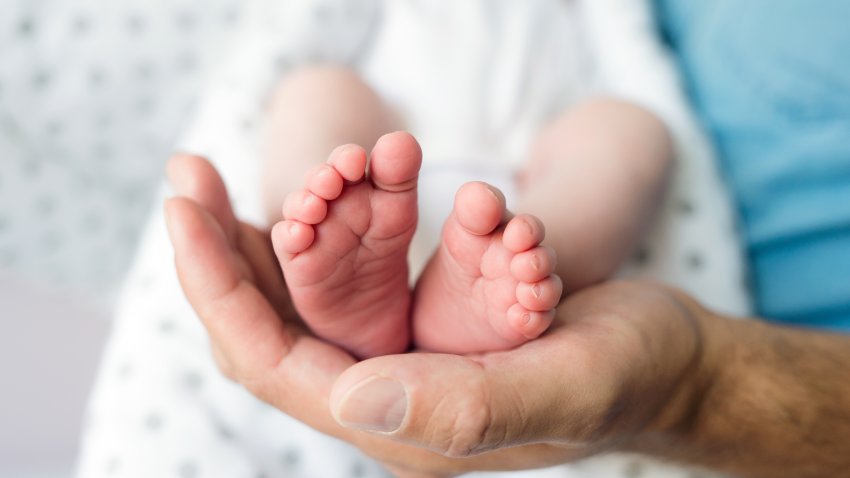 Unrecognizable father with newborn baby son, legs and hand. Close up.