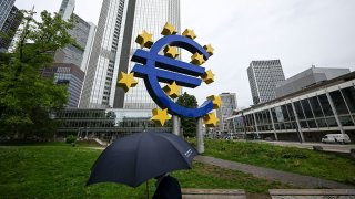 A man shelters from the rain under an umbrella as he walks past the Euro currency sign in front of the former European Central Bank (ECB) building in Frankfurt am Main, western Germany.