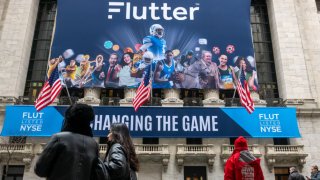 People walk by a banner outside of the New York Stock Exchange for the initial public offering of Flutter Entertainment, the parent company of FanDuel, on Jan. 29, 2024.