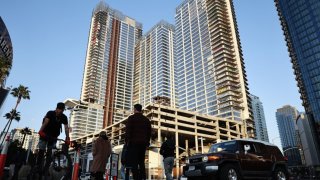 People pass beneath the so-called Graffiti Towers, where graffiti writers tagged 40 floors of an unfinished luxury skyscraper development last month, on March 20, 2024 in Los Angeles, California. Construction of the $1 billion Oceanwide Plaza luxury real estate development stalled in 2019 after a China-based developer ran out of funding leaving the three-tower project unfinished amid a housing crisis in the city. 