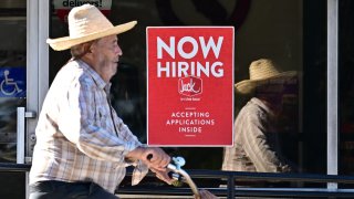 A cyclist rides past a “Now Hiring” sign posted on a business storefront in San Gabriel, California on August 21, 2024. 