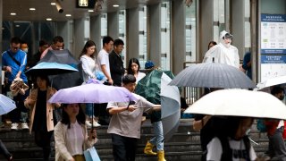 Local residents with umbrellas walk out of a metro station in rain during morning rush hour on September 20, 2024 in Beijing, China. 