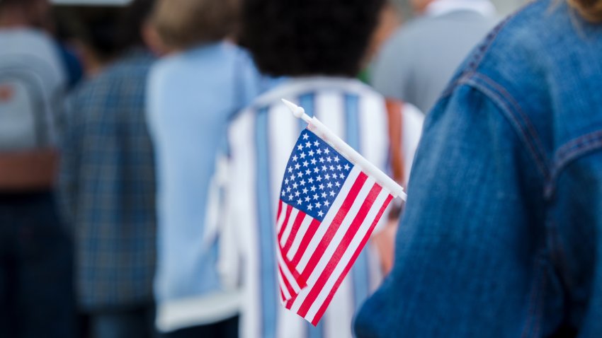 Woman holds US flag while waiting in line to vote at polling place. Focus is on the flag.