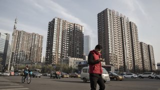 A pedestrian crosses a road in front of residential buildings in Beijing, China.