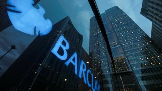 Signage shines through a window reflecting Barclays head office in Canary Wharf, London, U.K.