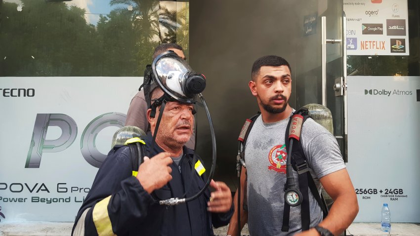 Firefighters stand outside a damaged mobile shop in Lebanon.