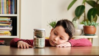 Child saving money in a glass jar at home