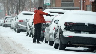A motorist clears snow off his vehicle parked along First Avenue as a winter storm sweeps over the intermountain West, plunging temperatures into the single digits and bringing along a light snow in its wake Saturday, Jan. 18, 2025, in Denver.