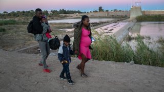 An immigrant family from Haiti walks toward a gap in the U.S. border wall
