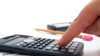 A finger adding up figures using a calculator isolated over a white background.