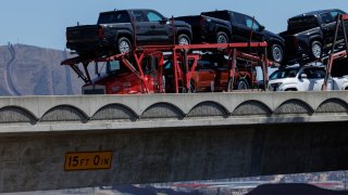The border wall is shown in a background as a semi-truck carrying Toyota trucks crosses a bridge after clearing U.S. Customs while entering the United States from Mexico along the border in San Diego, California, on March 4, 2025.