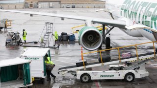 A ground operations employee unloads baggage from a Frontier Airlines Inc. plane on the tarmac at Denver International Airport (DIA) in Denver, Colorado.