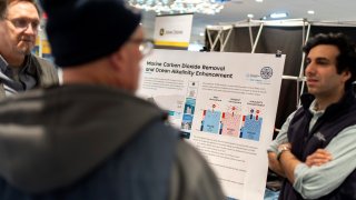 An information board is displayed by the Woods Hole Oceanographic Institution to educate the fishing community on an ocean carbon project as scientist Adam Subhas, right, and Ken Koster, left, director of research communication, talk with shell fisherman Alex Brown, at the Massachusetts Lobstermen's Association Annual Weekend and Trade Show, Friday, Jan. 31, 2025, in Hyannis, Mass.