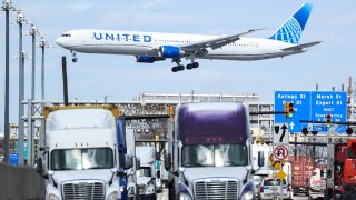 A United Airlines Boeing 767 passenger aircraft approaches Newark Liberty International Airport as trucks travel near the Port Jersey Container Terminal in Jersey City, New Jersey, on April 8, 2025.