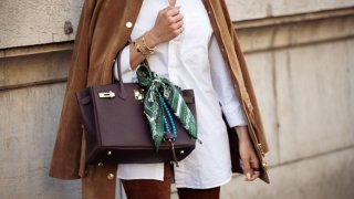 A guest wears white shirt, brown pants, brown suede jacket and brown Hermes bag with a green and white silk neck scarf outside the Hermes fashion show during the Womenswear Fall/Winter 2025/2026 as part of Paris Fashion Week on March 08, 2025 in Paris, France.