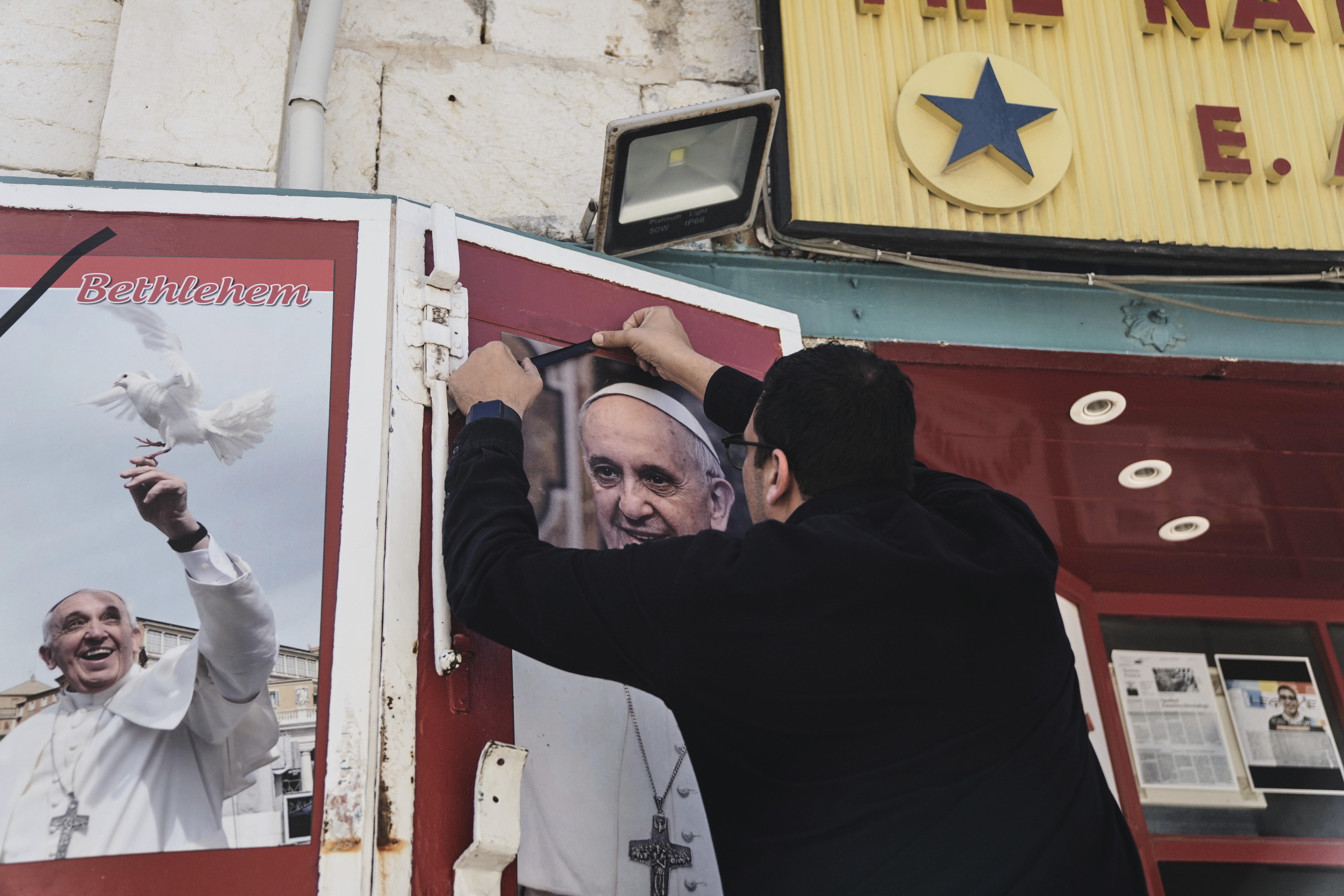 A shop owner places a black ribbon over a photo of the late Pope Francis after the news of his death, in Bethlehem, West Bank, on Monday, April 21, 2025.