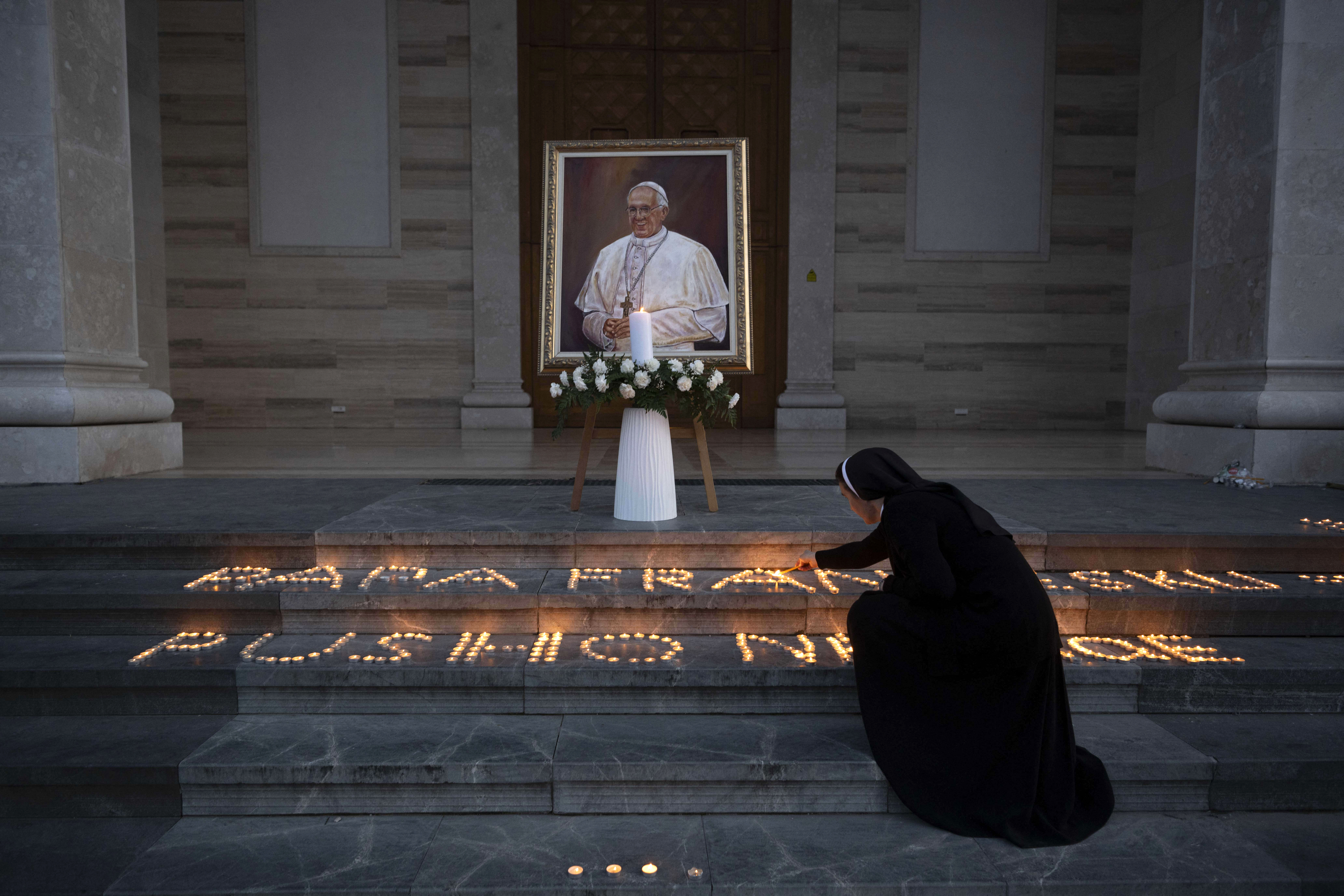 A Catholic nun lights a candle next to a portrait of the late Pope Francis displayed at the St. Mother Teresa Cathedral in Pristina on April 21, 2025.