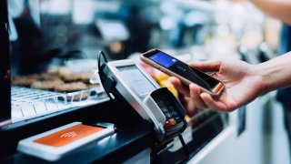 Close up of a woman’s hand paying with her smartphone in a cafe, scan and pay a bill on a card machine making a quick and easy contactless payment.
