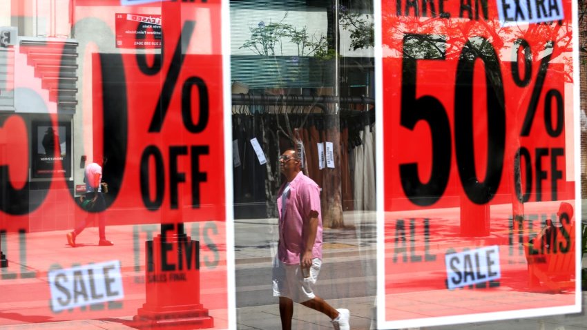 Visitors are caught in the reflection of a store offering 50% off on all items on the Third Street Promenade in Santa Monica on July 16, 2024. 
