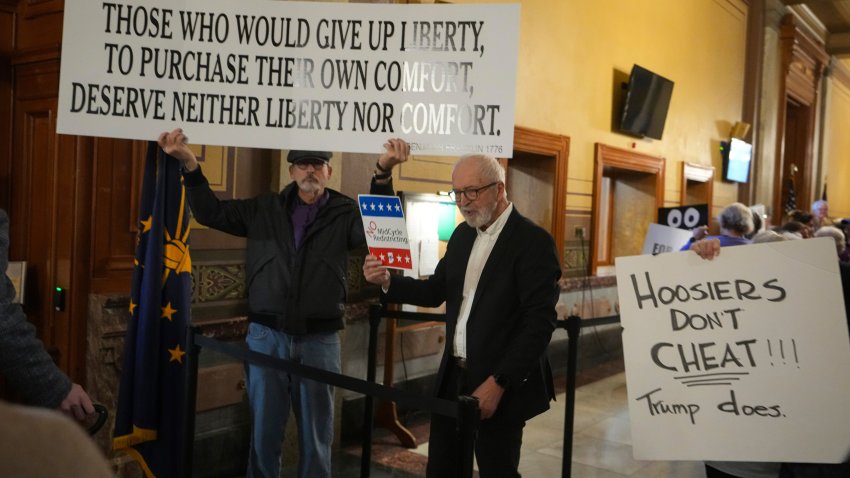 Protestors hold signs outside the Indiana Senate chamber before a vote to redistrict the state&#039;s congressional map at the Statehouse in Indianapolis, Thursday, Dec. 11, 2025.